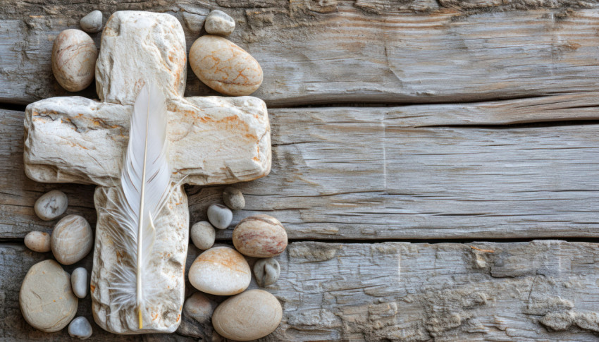White stone cross with feather and pebbles on wood background White stone cross with feather and pebbles on wood background