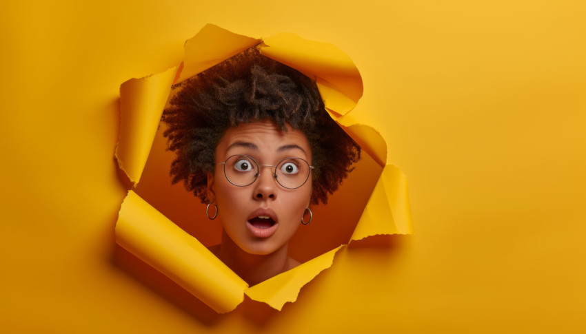 Surprised young woman emerges through yellow paper hole expressing amazement and curiosity in a whimsical setting Surprised young woman emerges through yellow paper hole expressing amazement and curiosity in a whimsical setting