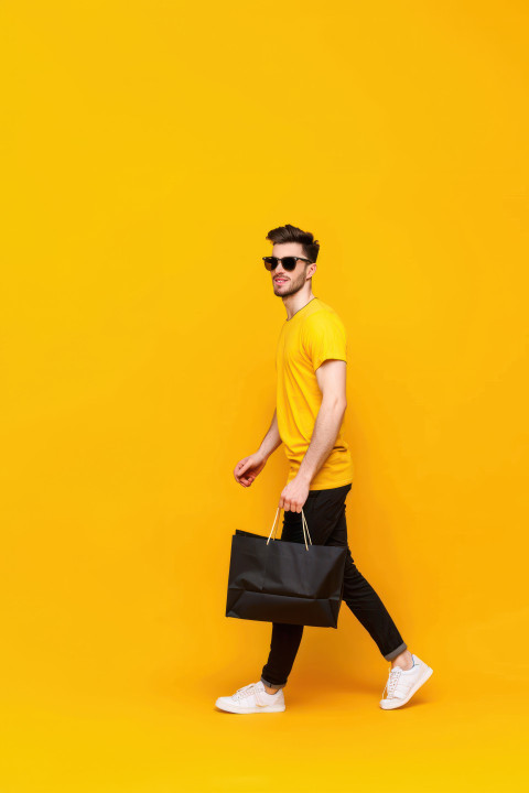 A man in sunglasses and a yellow t shirt carrying a black shopping bag representing black friday sales A man in sunglasses and a yellow t shirt carrying a black shopping bag representing black friday sales, black friday, shopping fashion