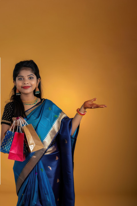 Indian woman in saree holding shopping bags and pointing at product against an isolated background Indian woman in saree holding shopping bags and pointing at product against an isolated background